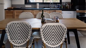 A kitchen with a wooden table and white wicker chairs, a microwave, and a window with a view of greenery.