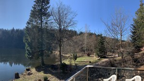 Une vue paisible sur un lac, avec une terrasse en bois, un mur de pierre et un ciel dégagé.