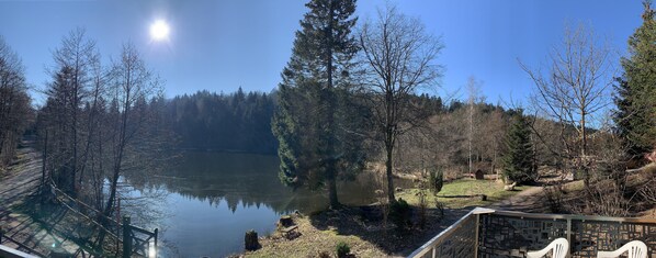 A serene lakeside view with a wooden deck, a stone wall, and a clear sky. - Small cottage in the heart of nature (Rupt-sur-Moselle)