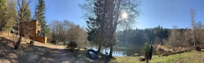 A rustic cabin with a wooden exterior, a dirt path leading to it, and a serene lake surrounded by trees. - Small cottage in the heart of nature (Rupt-sur-Moselle)