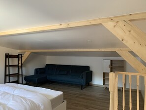 A loft bedroom with a wooden ceiling, a dark blue sofa, a white bed, and a wooden ladder. - Small cottage in the heart of nature (Rupt-sur-Moselle)