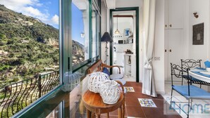 A balcony with a view of a mountainous landscape, a dining area with a table and chairs, and a kitchen visible through an open door. - Relaxing Positano (Positano)