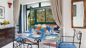 A dining area with a round glass table, blue placemats, and metal chairs. A window with curtains offers a view of greenery outside. - Relaxing Positano (Positano)
