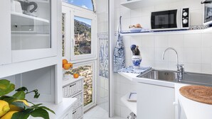 A kitchen with white cabinetry, a view of a mountainous landscape through a window, a microwave, and a sink. - Relaxing Positano (Positano)