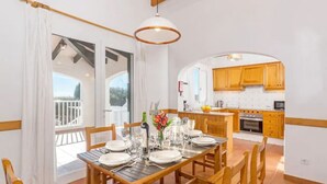 Un coin repas avec une table en bois dressée pour quatre personnes, une cuisine en arrière-plan et un balcon doté d’une balustrade blanche.