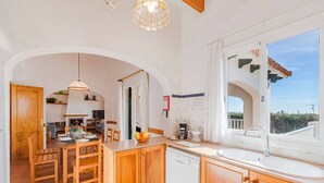 Une cuisine avec des meubles en bois, un évier blanc et un coin repas comprenant une table et des chaises.