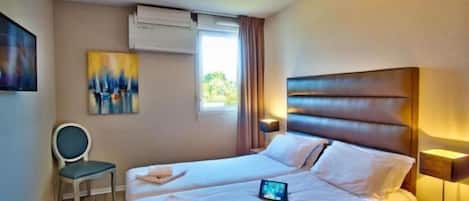 A hotel room with a bed, bedside table, lamp, chair, and artwork on the wall.