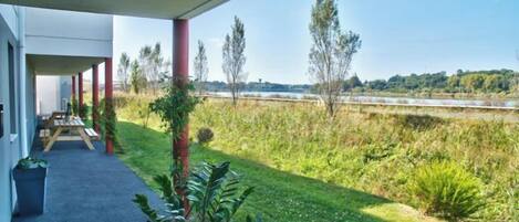 A covered outdoor area with a view of a grassy field and a body of water.