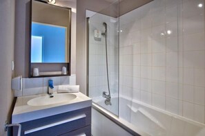 Un baño moderno con un lavamanos blanco, un espejo y una ducha con cerramiento de vidrio.