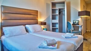 Une chambre d’hôtel avec un grand lit, une armoire, un bureau avec une chaise et une table de chevet avec une lampe.