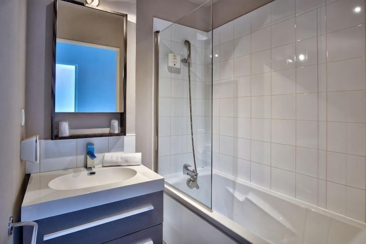 A modern bathroom with a white sink, mirror, and shower.