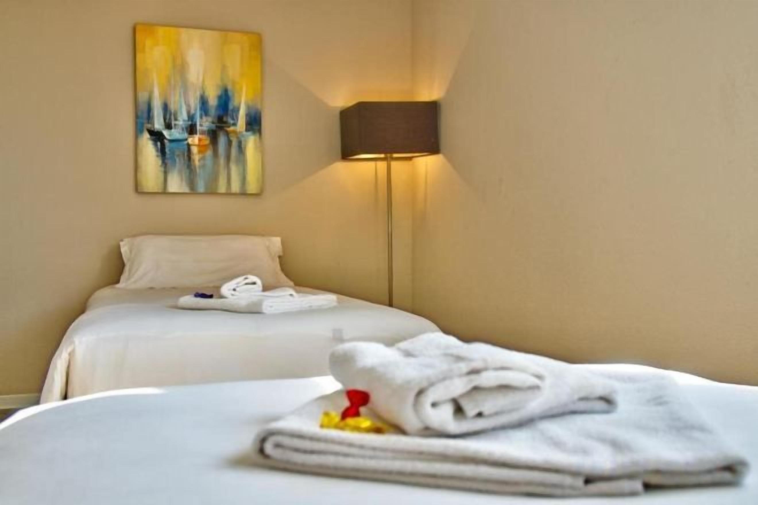 A hotel room with a bed, a painting on the wall, and a lamp.