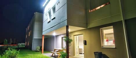 A modern building with a flat roof, a covered outdoor seating area, and a well-lit entrance.