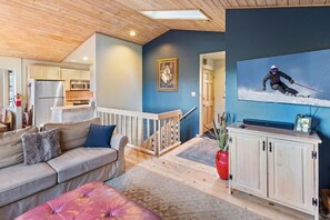 A living room with a sofa, ottoman, wooden cabinets, a painting, and a television.
