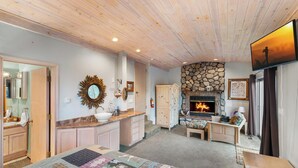Ein gemütliches Zimmer mit Kamin, Holzbalkendecke und einer Steudecke auf dem Bett.