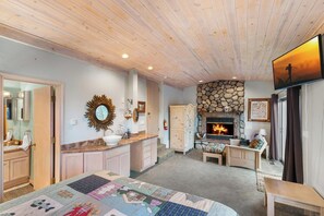 Une pièce chaleureuse avec une cheminée, un plafond en bois et une courtepointe sur le lit.