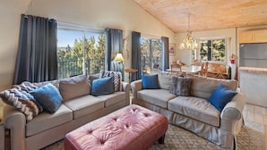 Ein gemütliches Wohnzimmer mit zwei Sofas, einem pinken Pouf und einem Essbereich mit Tisch und Stühlen.