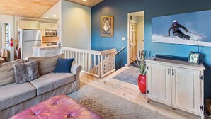 Ein Wohnzimmer mit Sofa, Hocker, einer Holztreppe und einem Fernseher, der einen Skifahrer zeigt.