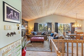 Una sala de estar acogedora con techo de madera, un sofá, una mesa de centro y un comedor con mesa y sillas de madera.
