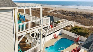 Ein zweistöckiges Haus mit einer Terrasse, die auf einen Strand und ein Schwimmbecken blickt.