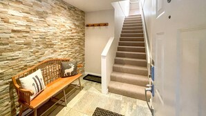 Una escalera con alfombra color beige que lleva a una puerta con el número 8. Un banco de madera con un cojín de ciervo está apoyado contra una pared de piedra.