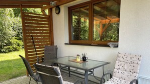 Eine Terrasse im Freien mit einem Glastisch, zwei Stühlen und einer Holzpergola.