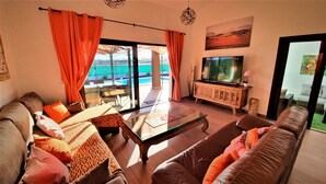 Un salon avec un canapé, une table basse en verre et un téléviseur. On peut admirer une piscine et un balcon depuis cet endroit.