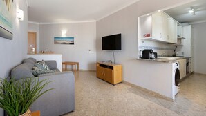 A living room with a sofa, a TV, a washing machine, and a small kitchen area. - Apartment 'Sunny Escape' with Sea View, Wi-Fi and Air Conditioning (Portimão)