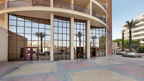 A hotel entrance with large glass doors, a curved balcony, and palm trees in the background. - Apartment 'Sunny Escape' with Sea View, Wi-Fi and Air Conditioning (Portimão)