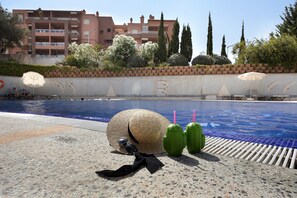 Un espace aménagé au bord de la piscine, comprenant une chaise longue, un parasol et un mur décoratif orné d’un motif en mosaïque.