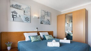 A bedroom with a wooden headboard, a bed with blue bedding, a nightstand with a plant, and wall art depicting nautical scenes. - Apartment 'Sunny Escape' with Sea View, Wi-Fi and Air Conditioning (Portimão)