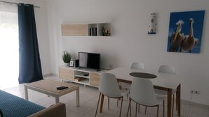 A modern living room with a TV, white chairs, a dining table, and a sofa. - Apartment "Ariana" with Pool, Wi-Fi, Balcony, Indoor Pool & Tennis Court (Portimão)