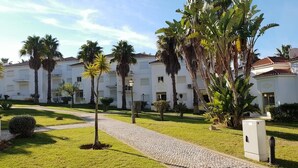 A hotel courtyard with a cobblestone path, palm trees, and a white building with balconies. - Apartment "Ariana" with Pool, Wi-Fi, Balcony, Indoor Pool & Tennis Court (Portimão)