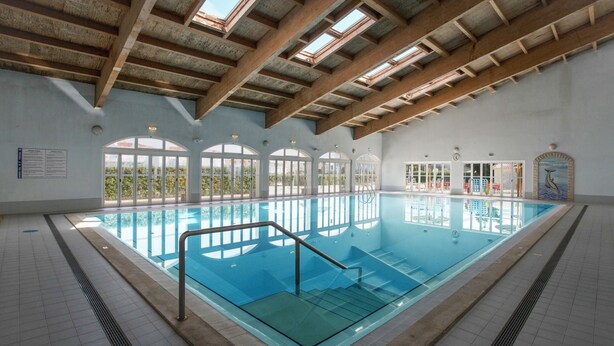 An indoor swimming pool with clear glass sides, wooden beams on the ceiling, and large windows. - Apartment "Ariana" with Pool, Wi-Fi, Balcony, Indoor Pool & Tennis Court (Portimão)