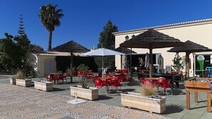 An outdoor patio area with red chairs and tables, a foosball table, and thatched umbrellas. - Apartment "Ariana" with Pool, Wi-Fi, Balcony, Indoor Pool & Tennis Court (Portimão)