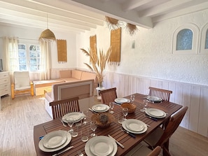 A dining area with a wooden table set for six, surrounded by wooden chairs.