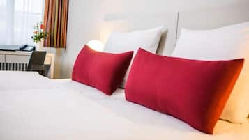 A hotel room with a neatly made bed, a desk with a chair, and a window with curtains.