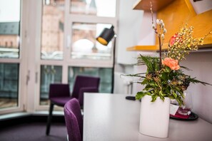 A modern hotel room with a large window, a purple chair, and a white vase with flowers on the table. - Erbacher Hof (Mainz)