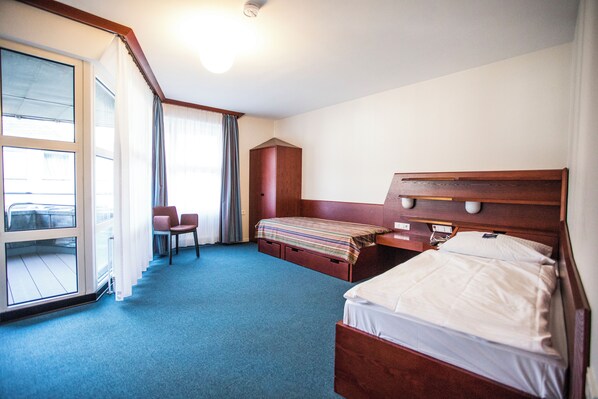 A hotel room with a large window, a bed, a desk, a chair, and a small cabinet. - Erbacher Hof (Mainz)