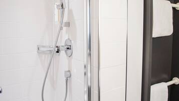 Une salle de bain moderne avec une douche à l’italienne en verre, des murs recouverts de carreaux blancs et une baignoire noire.