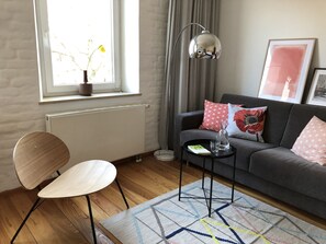 Ein modernes Wohnzimmer mit grauem Sofa, einem Holzstuhl, einem kleinen runden Tisch und einer Stehlampe.