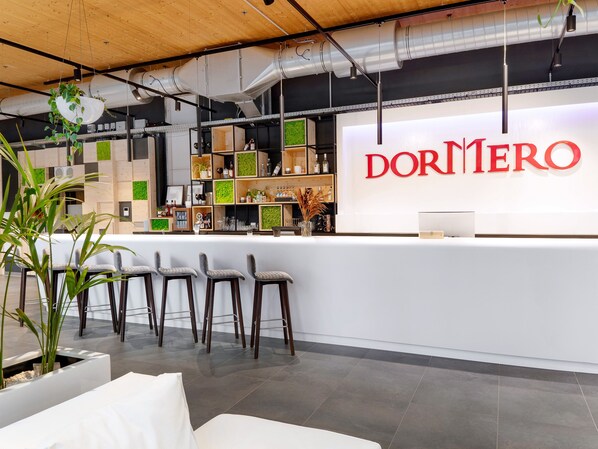 A modern bar area with a white counter, bar stools, and shelves stocked with bottles and glasses. - Dormero HoHo Wien (Vienna)