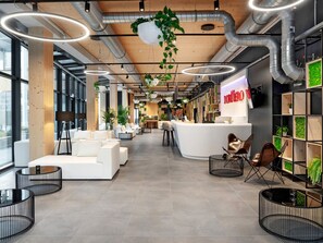 A modern office space with white sofas, a reception desk, and a green wall with plants. - Dormero HoHo Wien (Vienna)