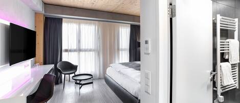 A modern hotel room with a wooden ceiling, a flat-screen TV, a desk with a chair, a bed, and a bathroom with a towel rack.