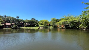 Ein ruhiger See mit klarer Spiegelung, umgeben von üppigem Grün und einigen Gebäuden im Hintergrund.