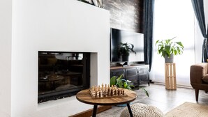 A modern living room with a fireplace, a TV, and a chessboard on a small table. - EL COLIBRÍ RURAL HOUSE  (Sanlúcar de Guadiana)