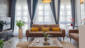 A modern living room with a brown sofa, a coffee table with decorative items, and a TV on the left. - EL COLIBRÍ RURAL HOUSE  (Sanlúcar de Guadiana)