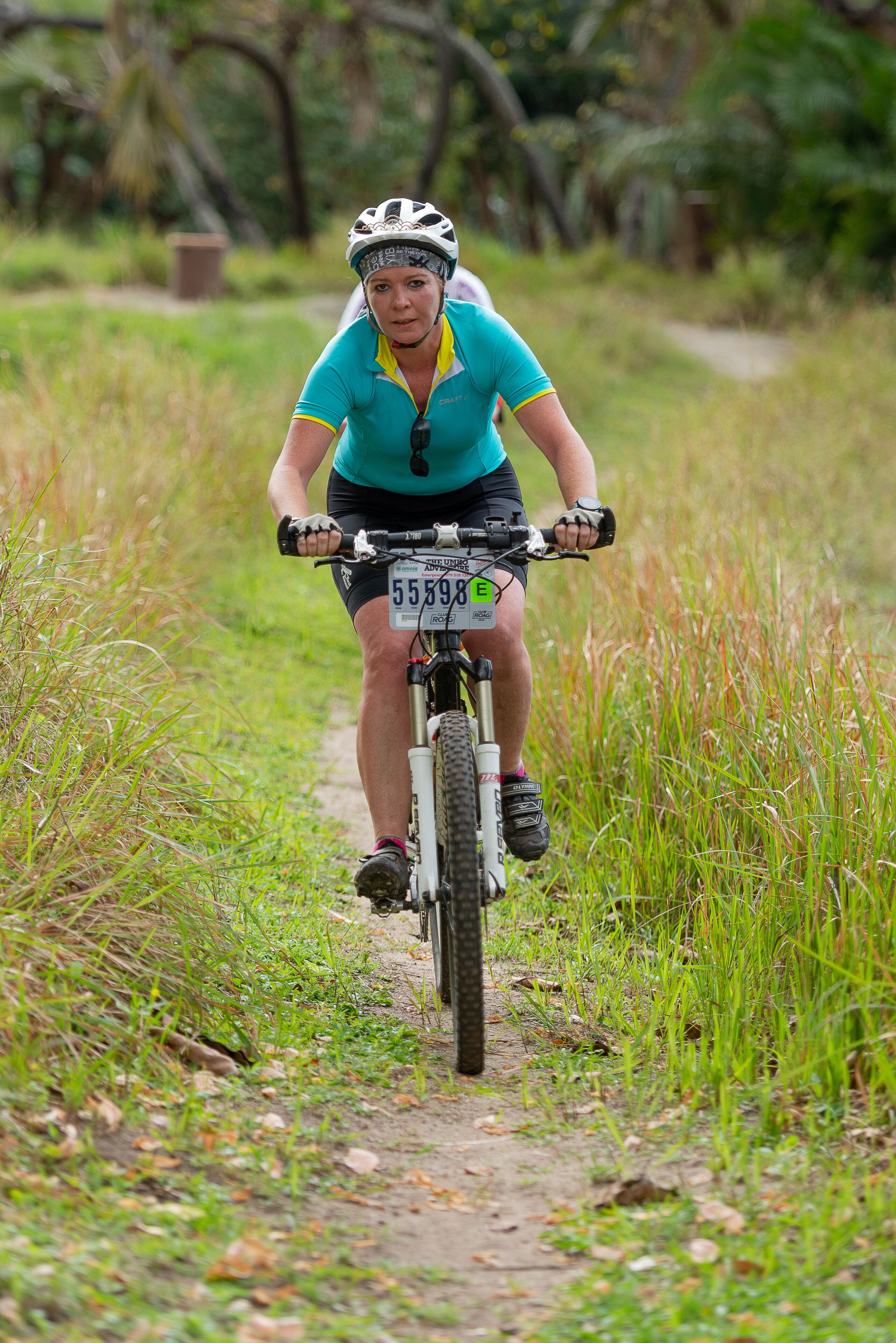 Une personne fait du vélo tout terrain sur un sentier de terre, entourée de verdure.