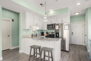 A kitchen with white cabinets, a stainless steel refrigerator, a microwave, and a stove. There are two stools at the island.