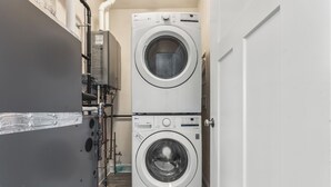 A laundry room with two stacked washing machines, a water heater, and a door leading to another room. - Beachside Abode 1A (Old Orchard Beach)